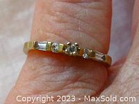 Close-up photo of a delicate vintage yellow gold ring on a finger, showing the front detail of small brilliant, round, and baguette cut diamonds prong set.