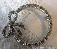 Front view of the circular marcasite brooch with bow detail showing marcasite stones and rhodium plating detail on lace background.