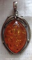 Close-up front view of oval amber pendant set in silver with floral open work design