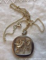 Photo of the sterling silver chain and pendant laid out on cloth, showing the chain and the front of the pendant with flower design in openwork style.