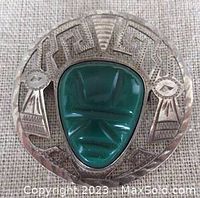 Front view of vintage sterling silver brooch with green carved mask stone and openwork Aztec design