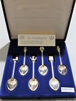 Six silver plated wedding spoons with distinct model-themed tops displayed in a blue velvet-lined gift box with cream inner lid lining. Label present with product information.