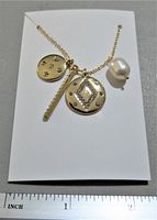 Front view of the necklace showing three pendants: a large fresh water pearl, a round gold-tone disc with diamond-shaped rhinestone pattern, a smaller round gold-tone disc with scattered rhinestones, and a slender textured bar pendant.