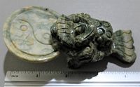 Stone carved Chinese good luck piece showing creature and circular base with Yin Yang symbol with inch ruler for scale.