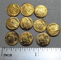 Top side view of 10 gold plated mini Maximillion coins laid out on a surface with a ruler showing size approximately 1 inch diameter each.
