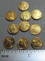 Ten gold plated mini Maximillion coins arranged on flat surface with ruler for scale showing each coin about 1 inch diameter.