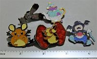 Front view of all 5 enamel collector pins showing Pokémon characters and Alice in Wonderland themed pins arranged in a line with ruler for scale.