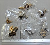 Lot of seven pairs of cufflinks and one tie pin individually bagged, placed on a gray surface with a ruler for size reference.