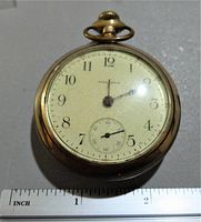 Front face of the pocket watch showing white dial, black numerals, and subdial for seconds. Scale shows approx 2 inches diameter.
