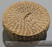 Top view of closed small handmade woven basket with ruler showing approximately 3 inches diameter.