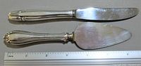 Two small silverware items side by side with a ruler showing size, a knife and a pie server with detailed sterling silver handles.