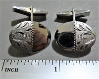 Front side view of the pair of vintage sterling silver cufflinks showing the oval shape, polished surface and engraved decorative motifs with a beaded border.