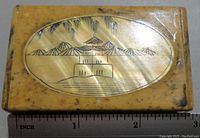 Top view of rectangular stone trinket box lid showing carved and etched Chinese style pagoda, mountains, and tree pattern with ruler for scale.