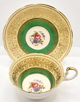 Tea cup and saucer set with floral center, green band, and gold leaf pattern detailing