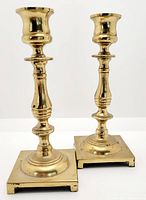 Pair of brass candlesticks with polished finish and square bases, showing age related wear.