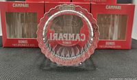 Bottom view of a Campari Negroni lowball glass showing embossed CAMAPRI logo and faceted bottom design.