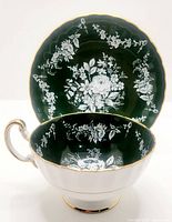 Photo of Aynsley bone china cup and saucer showing the deep green background with white floral design and gold trim.