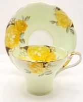 Corset-shaped cup and matching saucer set decorated with yellow roses and gold trim, shown front view.