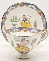 Tea cup and saucer front view showing lady and floral designs with gold trim.