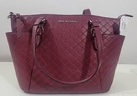 Front view of the burgundy Dana Buchman Cherry Tote handbag showing embossed pattern, brand name plate, handles, and side pockets.