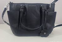 Front view of a black Dana Buchman handbag with dual handles and flower charm, showing texture and overall appearance.