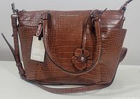 Front view of the cherry color Dana Buchman tote handbag with crocodile pattern, brand name plate, flower charm, and attached tag.