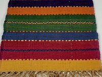 Photo showing section of the rug with multicolored horizontal stripes including navy, orange, green, blue, red, and gold with natural jute fringe edge.