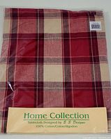 Folded and packaged red plaid round tablecloth with a beige Home Collection label, showing 100% cotton and designer information.