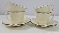 Four vintage cups and saucers stacked in two pairs, cream color with black dotted edge pattern.