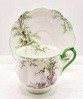 Tea cup and saucer showing the detailed Greenwood Tree pattern, green handle and rim on cup, scalloped saucer with matching design.