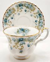 Tea cup with matching saucer behind, showing floral and gold design around rim and cup body.
