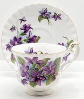 Tea cup and saucer displayed with floral pattern of purple flowers and green leaves, gold trim visible