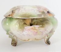 Porcelain RS Prussia hair receiver with hand-painted floral design and three legs, visible detailed view showing ornate scalloped lid and painted flowers.