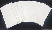 Twelve white folded dinner napkins arranged side by side on black background