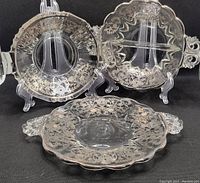 Three vintage glass pieces with silver overlay displayed on stands: a small bowl, divided bowl, and serving plate, showing overall design and size.