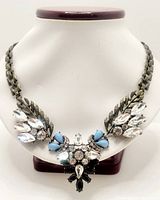 Front view of the vintage statement necklace on display bust, showing the full design with metallic leaves and multi-colored rhinestones including clear, light blue, and black stones.