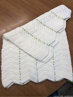 Photo of a white crocheted baby blanket with green ribbon trim laid on a wooden surface.