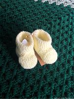 Close-up photo of a pair of pale yellow hand-knitted baby booties placed on a green crocheted blanket.