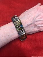 Metal stretch bracelet on wrist showing detailed floral and scroll patterns with colorful enamel accents.