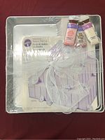 A set of three square Wilton cake pans wrapped together with decorative items including colored sugar and white netting to show complete lot contents