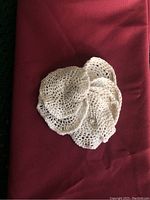 Photo shows a stack of six white crocheted round coasters with scalloped edges placed on a red fabric surface.