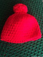 Photo showing a bright red crocheted toque with a pom-pom, highlighting the textured stitch pattern and craftsmanship.