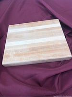 Top view of handcrafted solid wood cutting board showing smooth finish and natural wood grain pattern on a burgundy fabric background.