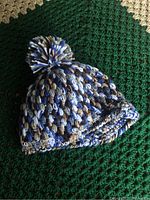 Close-up photo of handcrafted multi-coloured knitted toque with pom pom seen from side, showing textured knit and color pattern.