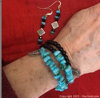 Close-up of a wrist wearing the turquoise and black coil bracelet with matching earrings laid beside it on a red fabric background.