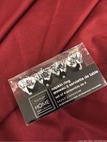 Box of 4 clear acrylic napkin rings with diamond-like facets, labeled Harman Home Table Collection, item dimensions included on box.