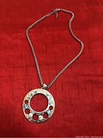 Full view of a silver necklace with a circular pendant featuring embedded clear and blue stones in a pattern.
