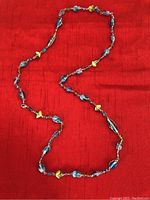 Photo showing the full length of the necklace laid flat on a red background, highlights the shape and color of the beads.