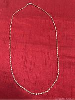 Full view of the gold colour necklace chain laid flat on a red textured background, showing the entire length of the chain.