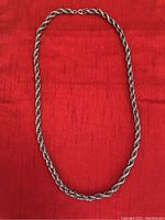 Full view of the 28-inch silver tone rope effect necklace laid flat on a red fabric background.